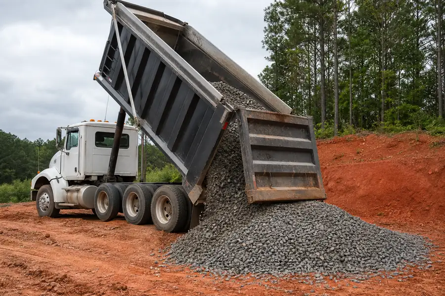 Dump truck delivering ABC stone for a North Carolina driveway base near red clay soil