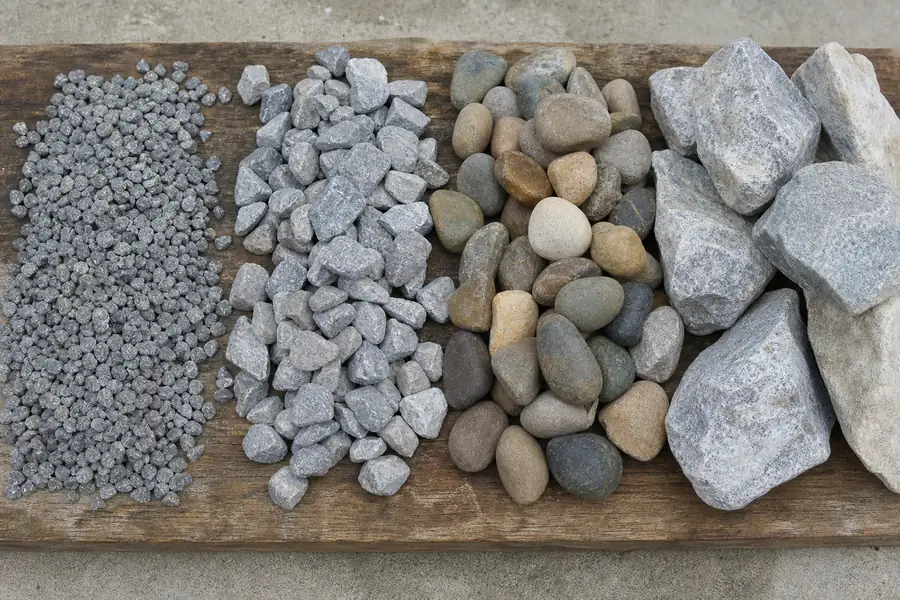 Comparison of drainage stones laid out on a board: #57, drain rock, river rock, riprap