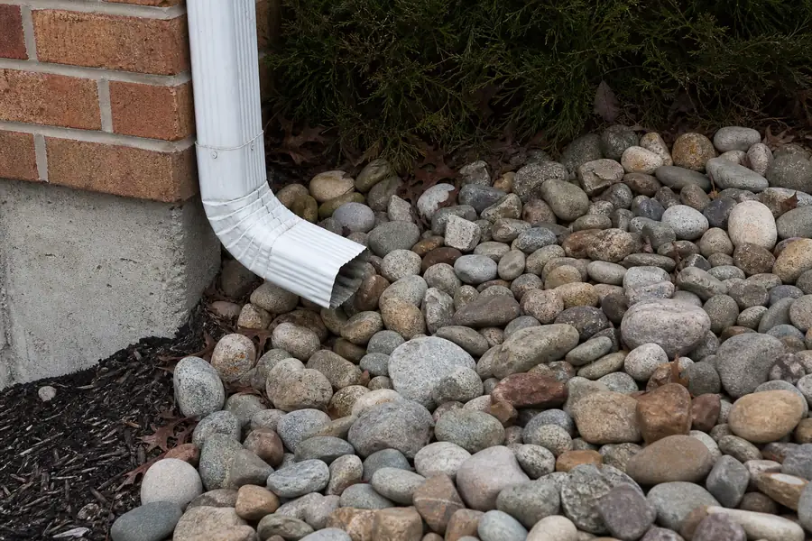Downspout emptying onto a bed of river rock beside a house