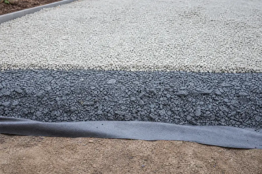 Cross-section diagram style photo of driveway layers: geotextile, compacted base, top stone