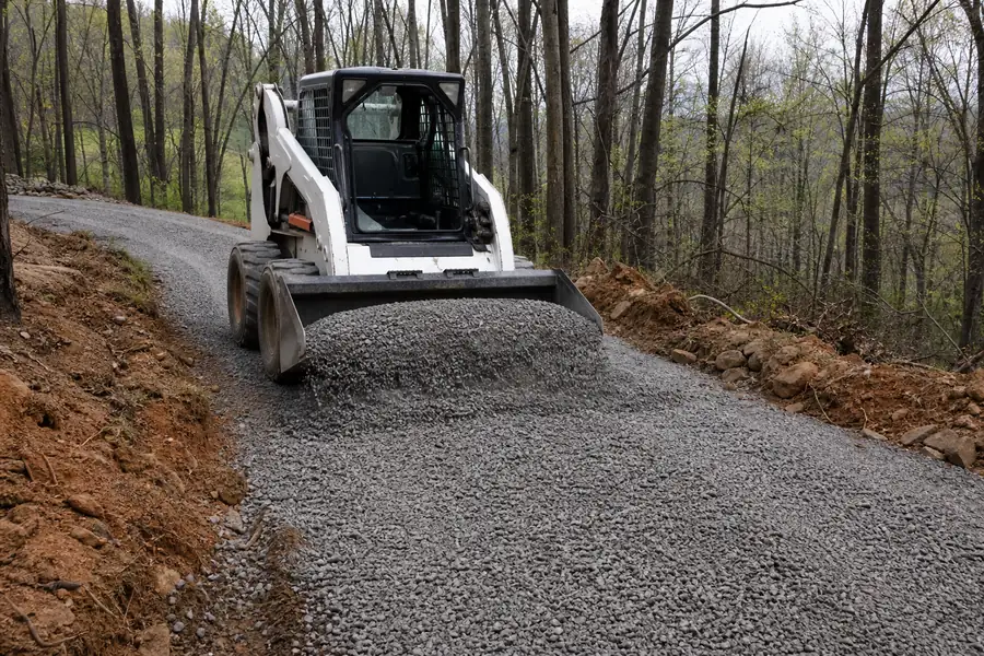 Skid steer spreading crusher run along a newly excavated driveway in a wooded lot