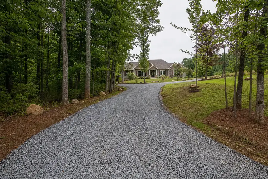 Finished gravel driveway curving toward a North Carolina house lined with trees