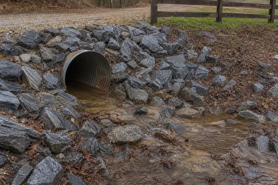 Riprap-armored culvert outlet beside a rural North Carolina driveway after rain